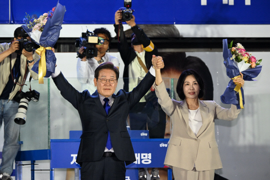 제21대 대통령 당선이 확실시되는 이재명 더불어민주당 대선 후보와 부인 김혜경 여사가 4일 국회 인근에서 당 주최로 열린 국민개표방송 행사에 참석해 박찬대 상임총괄선대위원장과 정은경 총괄선대위원장단으로부터 꽃다발을 받은 뒤 시민들을 향해 두 팔을 들어 인사하고 있다. [공동취재]